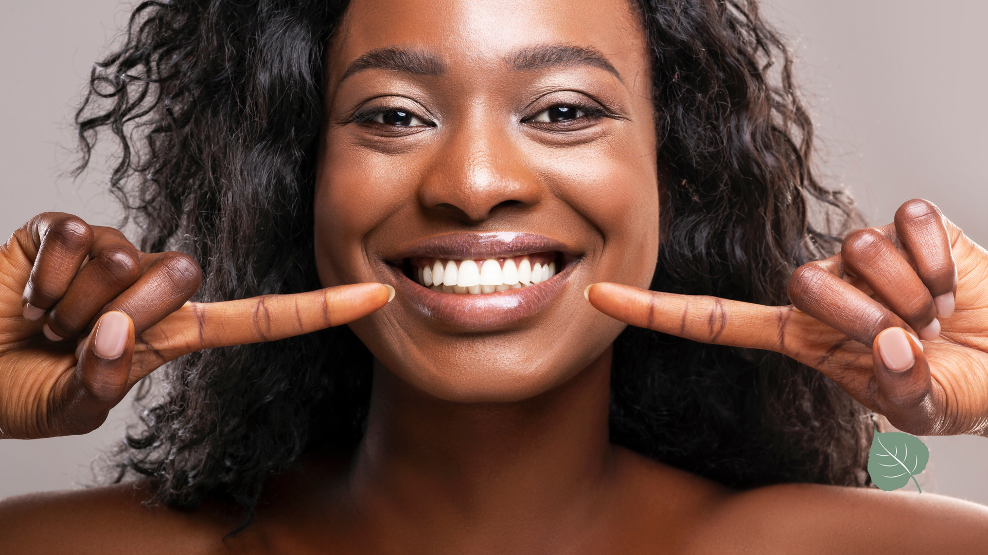 A woman is smiling and pointing at her teeth with her fingers.