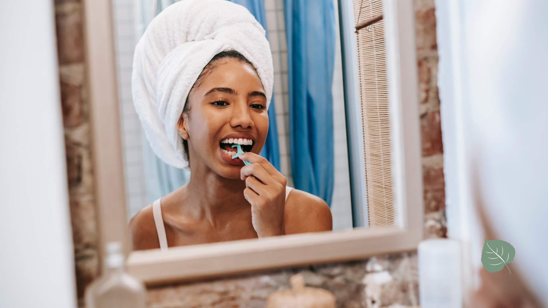 A woman with a towel wrapped around her head is brushing her teeth in front of a mirror.