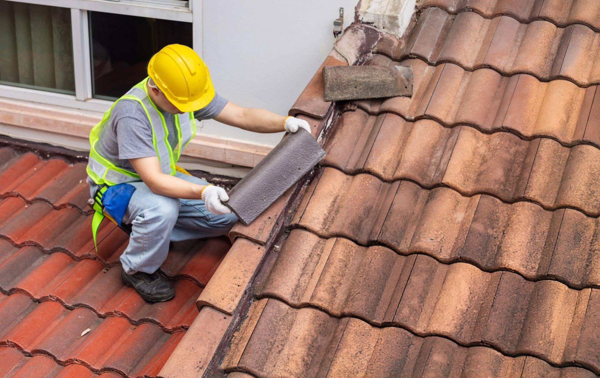 A man installs red tiles on a roof, demonstrating skilled work as a roof replacement contractor.