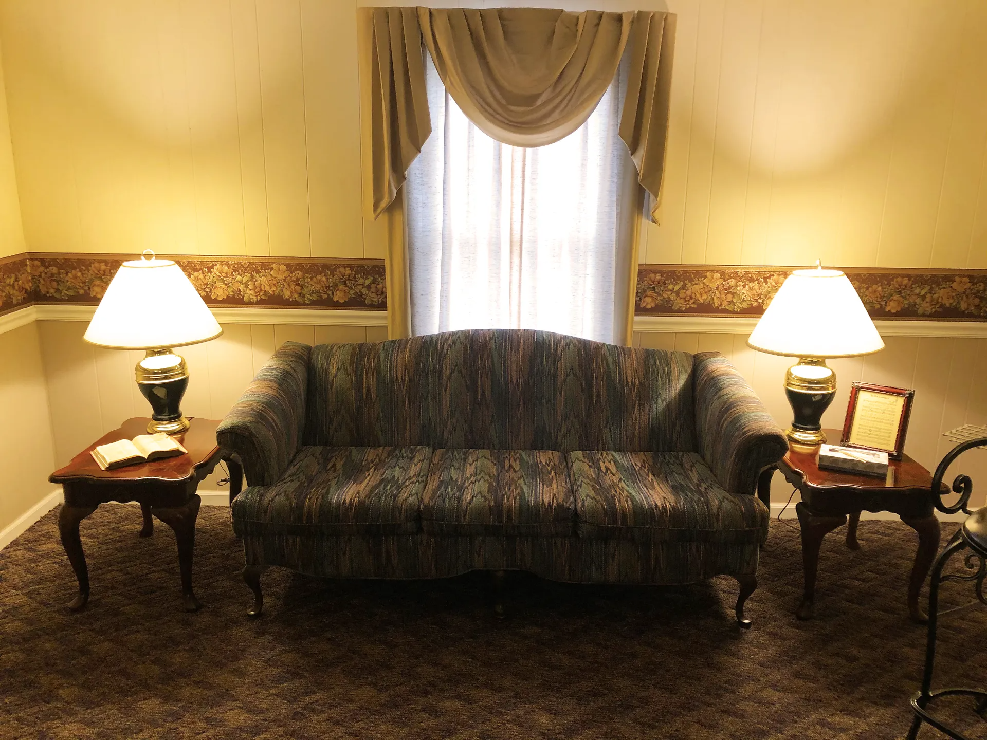 A living room with a patterned sofa, two lamps, side tables, and a window with curtains.