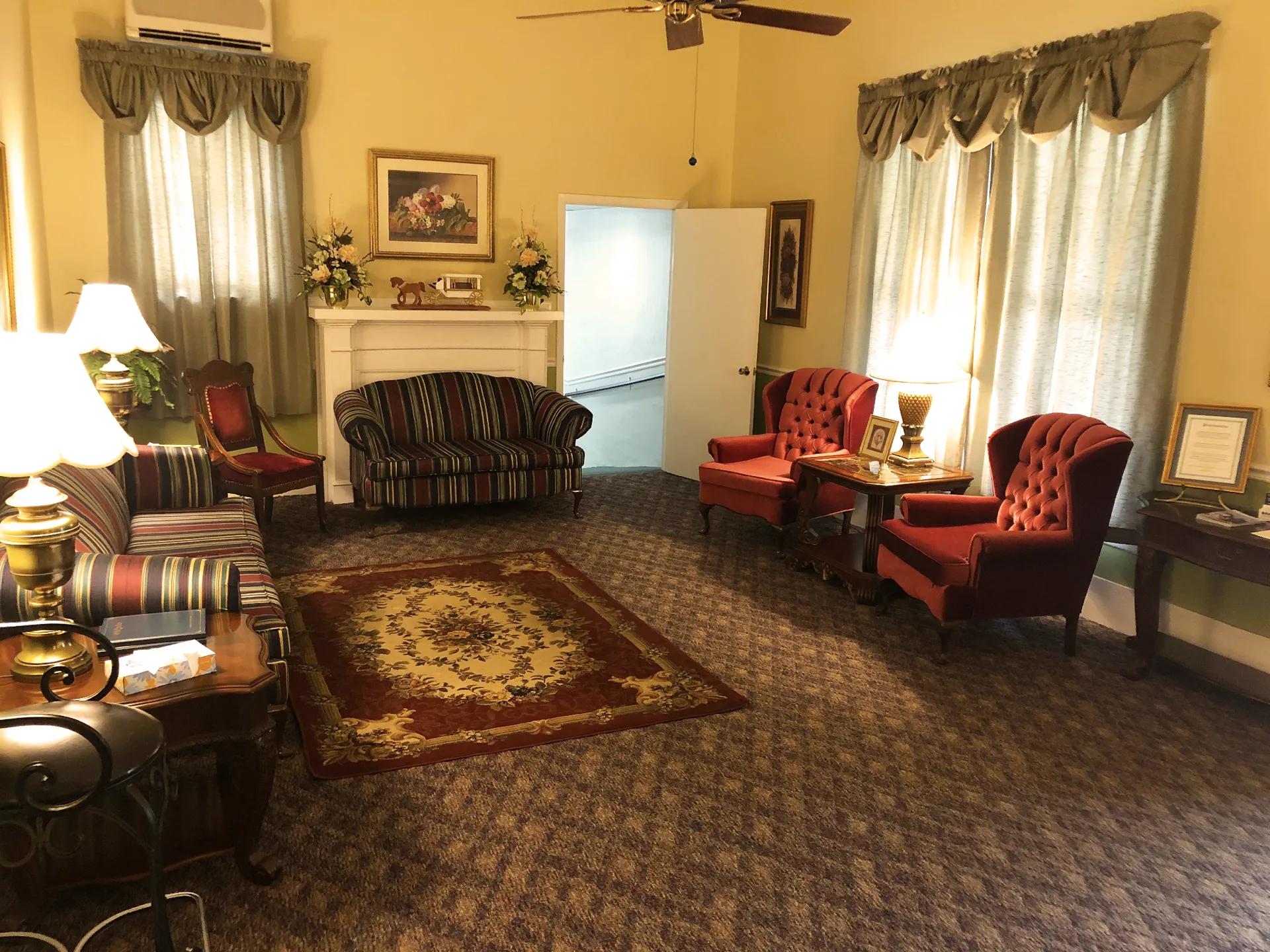Cozy living room with floral rug, ornate furniture, fireplace, and two windows with curtains.