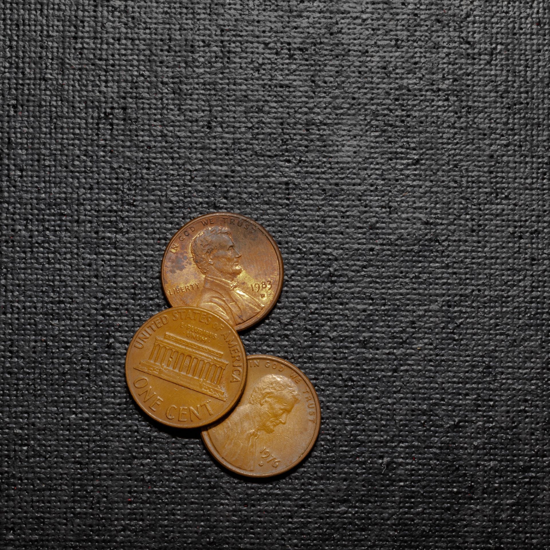 Three U.S. pennies on a textured black surface. Two are showing Lincoln's profile; one shows the Lincoln Memorial.