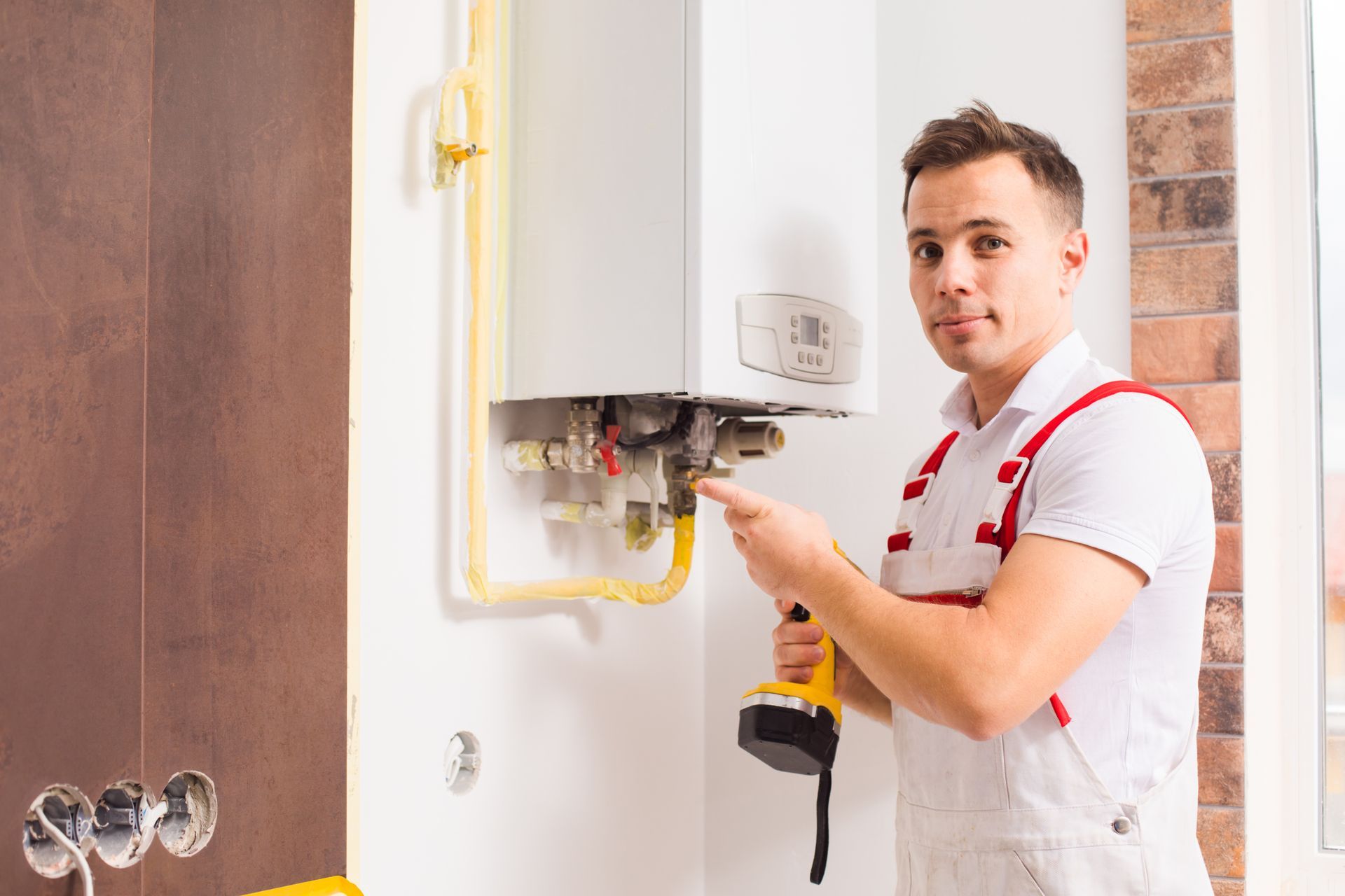 A man is fixing a boiler with a drill.