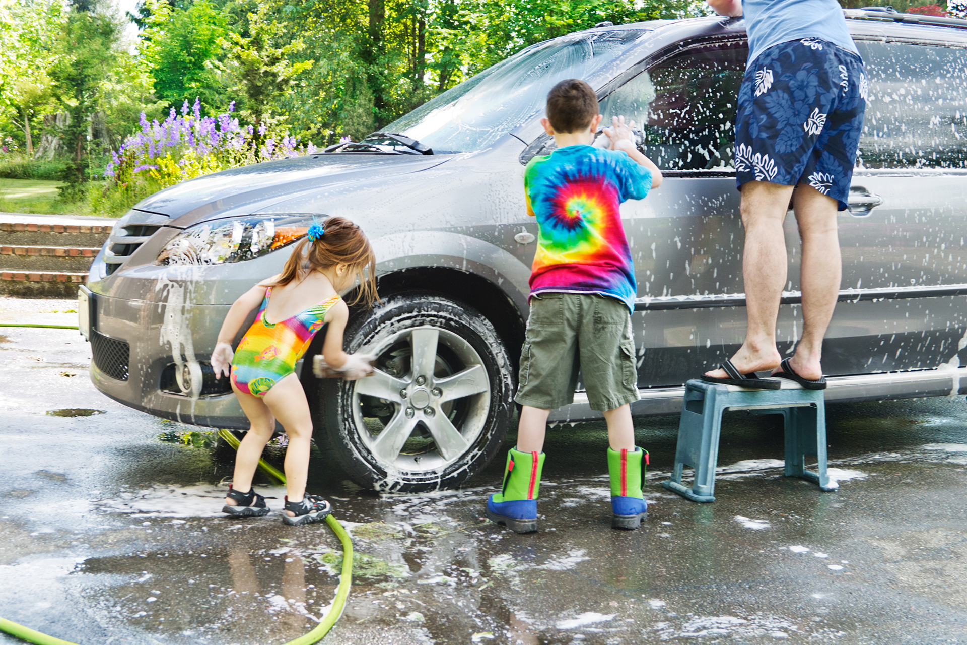 A man and two children are washing a car in a driveway.