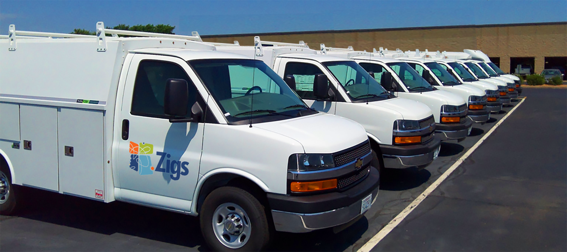A row of white vans are parked in a parking lot