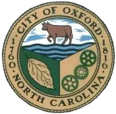 The seal of the city of oxford north carolina shows a cow standing on top of a box in the water.
