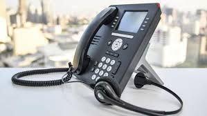 Black office phone with headset, on a white desk, with a cityscape background.