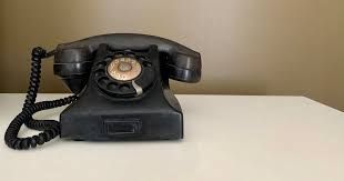 Black rotary phone on a white surface with a tan wall in the background.