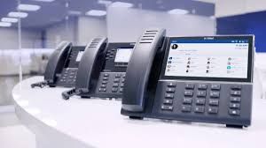 Three black office phones on a white counter; one phone displays a user interface on its screen.