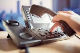 Hand dialing a black office phone.