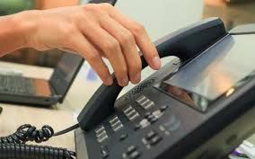 Hand lifting telephone receiver from a desk phone, ready to make a call.