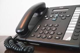 Black office telephone with a handset, number pad, and buttons, on a wooden surface.