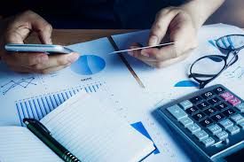 Person holding phone and card over financial documents, calculator, glasses and pen.