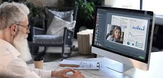An older person in a video call with a person on a computer, sitting at a desk.