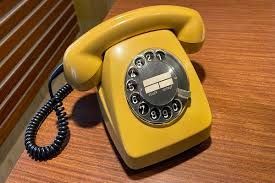 Yellow rotary phone on a wooden surface; black coiled cord and dial with numbers.