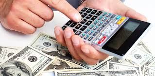 Person calculating money with a calculator on top of a pile of American dollar bills.