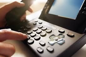 Person dialing a black phone with a finger pressing a button.