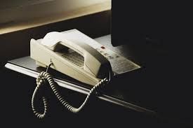 Off-white telephone on a dark surface, with coiled cord.
