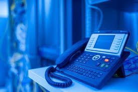 VoIP phone on a shelf in a server room, blue tones.