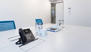 Conference room with white table, phone, water bottles, and blue chairs.