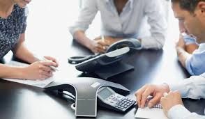 People in a meeting at a table, using a conference phone.