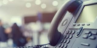Close-up of a black office telephone with a blurry background of people and lights.