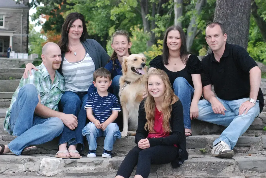 Family portrait on stone steps with a golden retriever, outdoors among trees and greenery