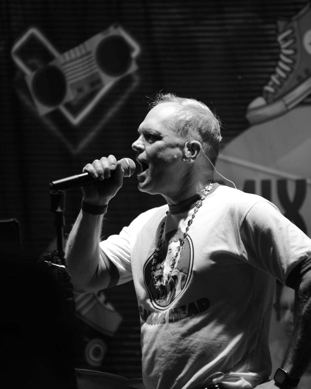 Singer holding a microphone onstage under bright lights, performing in black and white.