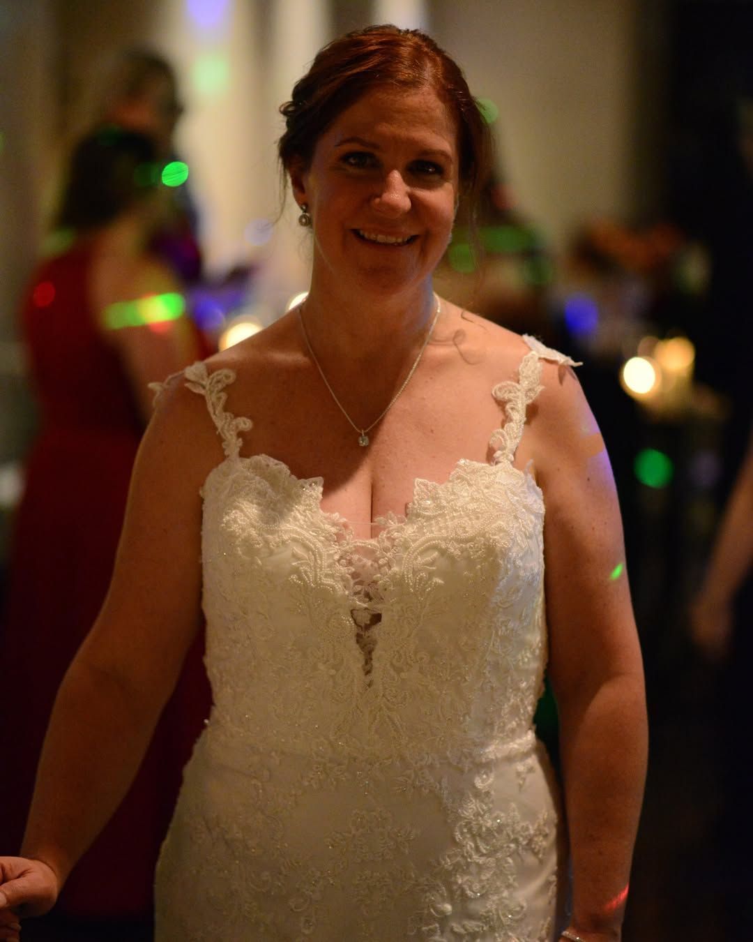 Smiling woman in a white lace dress at a dimly lit event with colorful lights in the background
