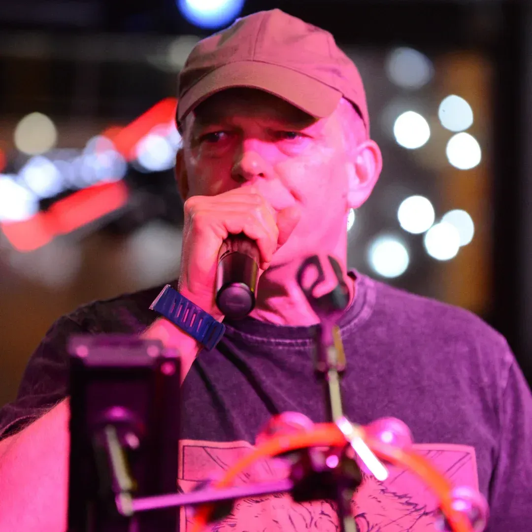 Singer in a cap performing into a microphone under pink stage lighting