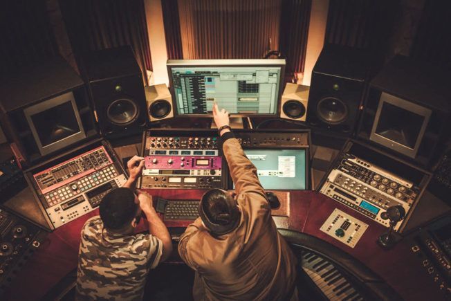 Two men are working on a computer in a recording studio.