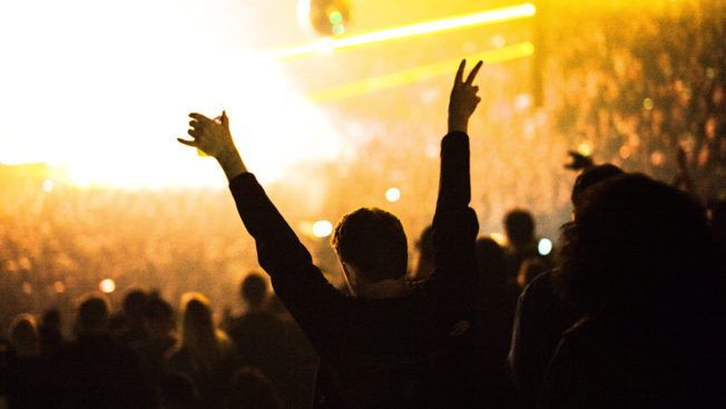 A crowd of people at a concert with their arms in the air.