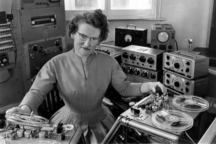 A woman is sitting in front of a tape recorder in a black and white photo.