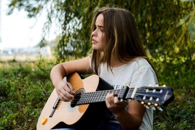 A woman is sitting in the grass playing an acoustic guitar.