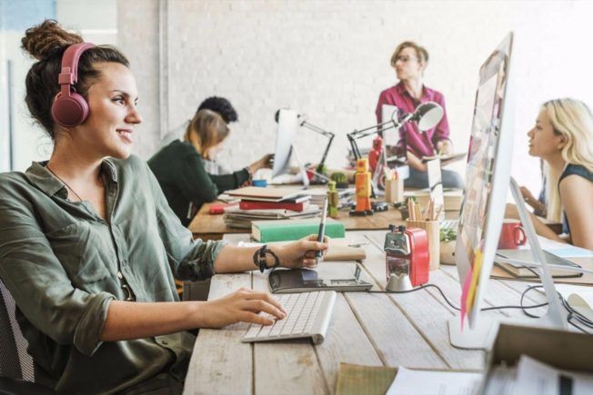 A woman wearing headphones is sitting at a desk in front of a computer.