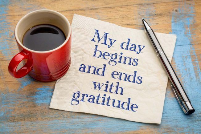 A napkin that says `` my day begins and ends with gratitude '' next to a cup of coffee and a pen.