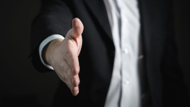 A man in a suit is reaching out his hand to shake someone 's hand.