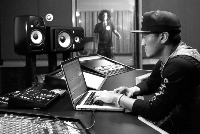 A man is typing on a laptop in a recording studio