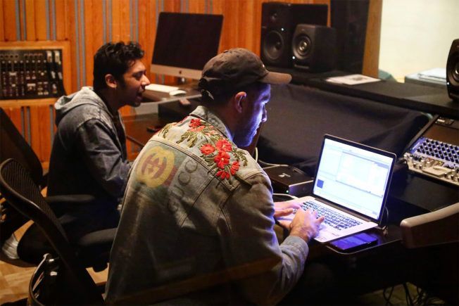 Two men are working on a laptop in a recording studio.