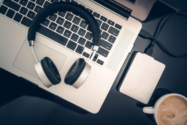 Headphones are sitting on top of a laptop next to a cup of coffee