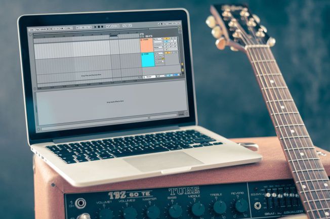 A laptop is sitting on top of an amplifier next to a guitar.