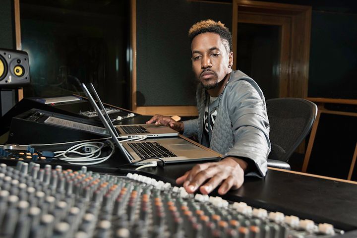 A man is sitting at a desk in a recording studio using a laptop and a mixer.