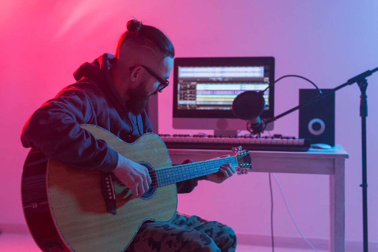 A man is sitting at a desk playing an acoustic guitar.