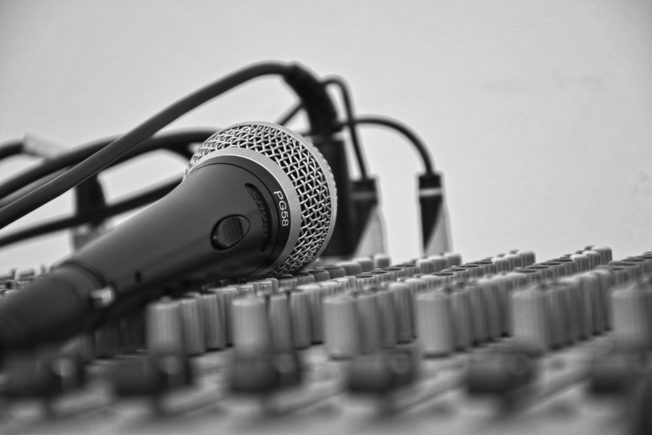 A microphone is sitting on top of a mixer in a black and white photo.