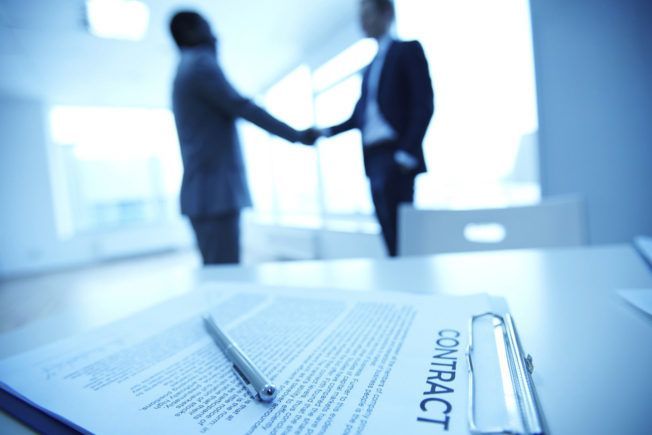 Two men shaking hands in front of a clipboard that says contract