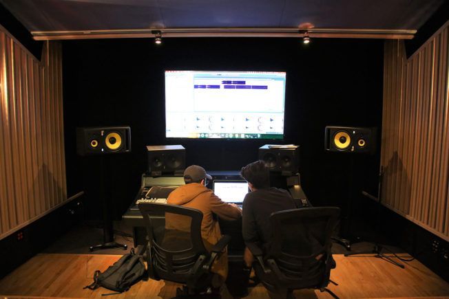 Two men are sitting in front of a computer in a recording studio.