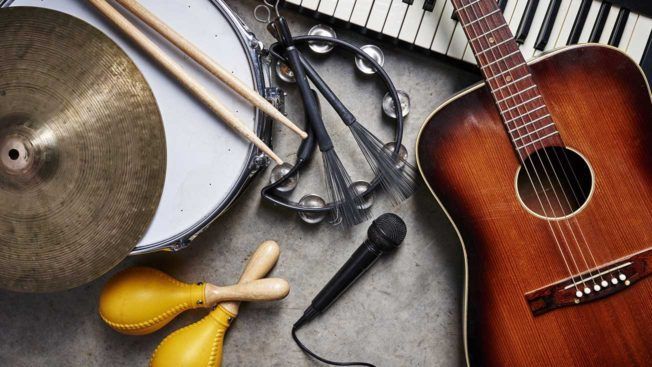 A guitar , drum , keyboard , microphone , tambourine and cymbals are on a table.