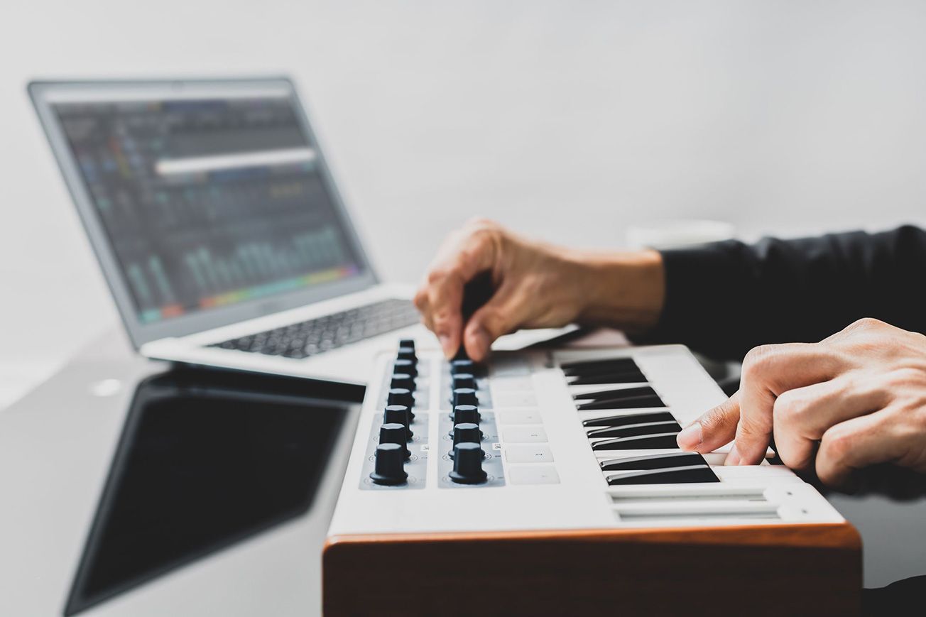A person is playing a keyboard in front of a laptop.