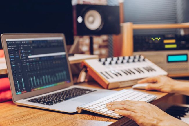 A person is typing on a laptop computer in a recording studio.