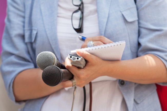 A woman is holding two microphones and a notebook in her hands.